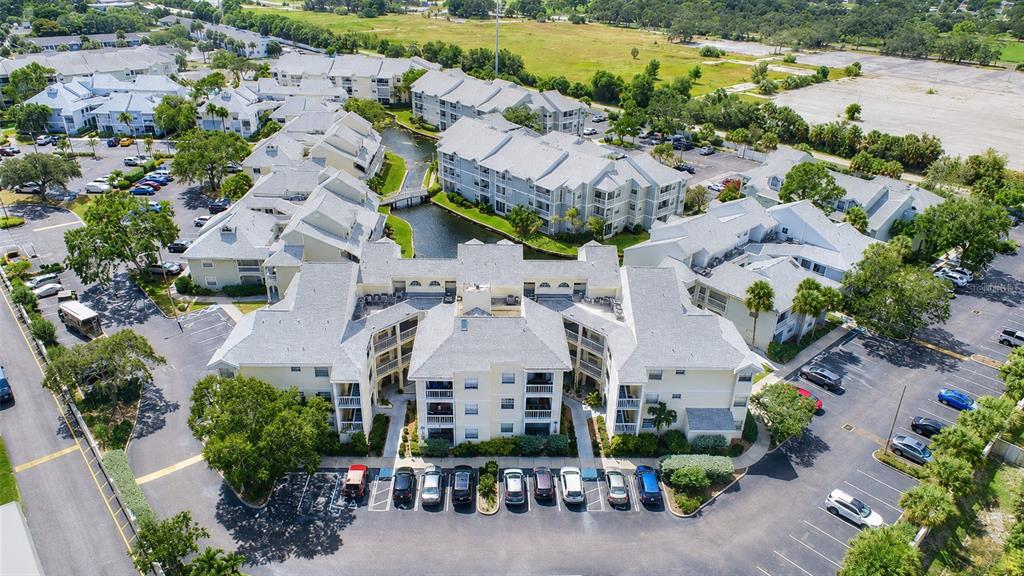 An aerial view shows a multi-story apartment complex with light-colored buildings, parking lots, and a canal — 6817 STONES THROW CIRCLE N UNIT 17208, ST PETERSBURG, FL