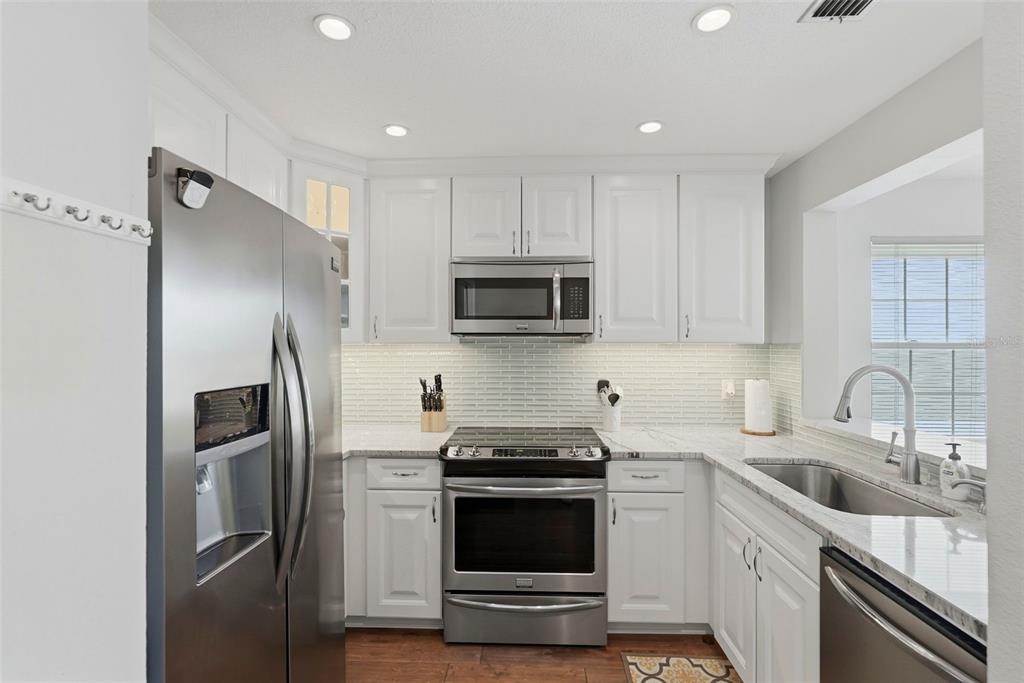 A modern kitchen features white cabinets, stainless steel appliances, a tiled backsplash, and granite countertops — 6817 STONES THROW CIRCLE N UNIT 17208, ST PETERSBURG, FL