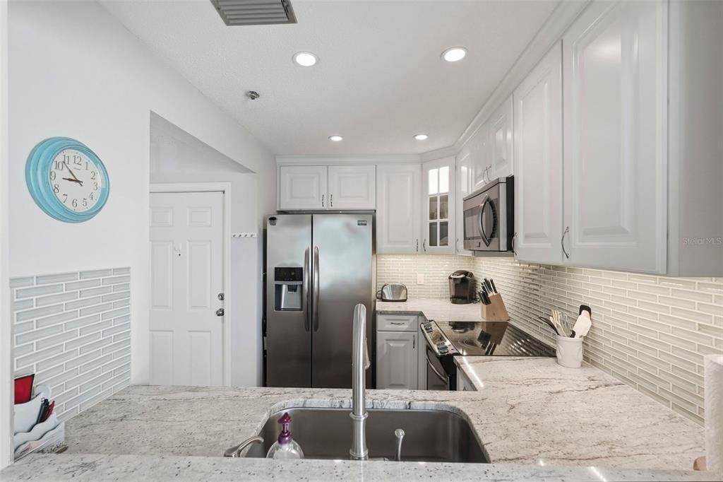 A kitchen features white cabinets, stainless steel appliances, a granite countertop, and a tile backsplash — 6817 STONES THROW CIRCLE N UNIT 17208, ST PETERSBURG, FL