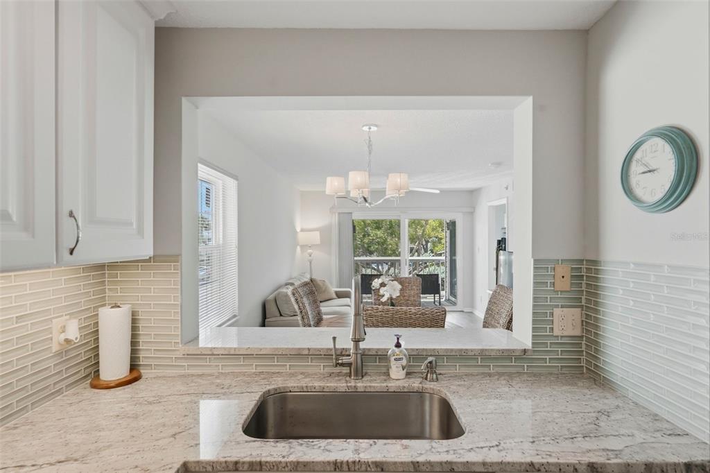 A kitchen sink with granite countertops overlooks a living room and a balcony with trees — 6817 STONES THROW CIRCLE N UNIT 17208, ST PETERSBURG, FL
