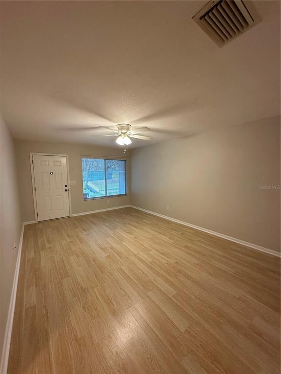 An empty room features light wood-look flooring, a ceiling fan, and a white entry door — 3125 VILLA ROAD, SEBRING, FL