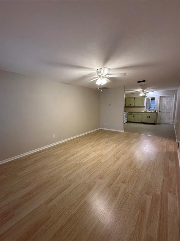 A spacious living room with light wood-look flooring leads into a kitchen with green cabinets — 3125 VILLA ROAD, SEBRING, FL