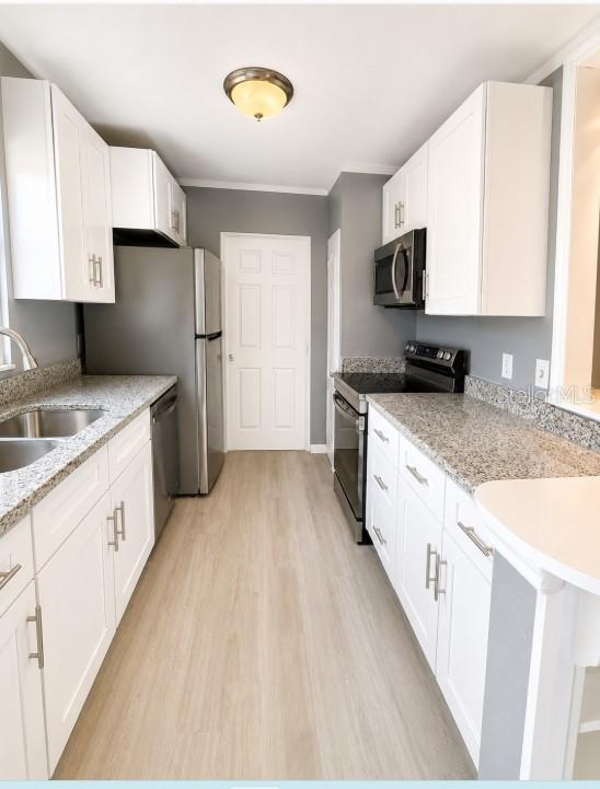 A galley kitchen features white cabinets, granite countertops, stainless steel appliances, and light wood flooring — 130 E DICIE AVENUE, EUSTIS, FL