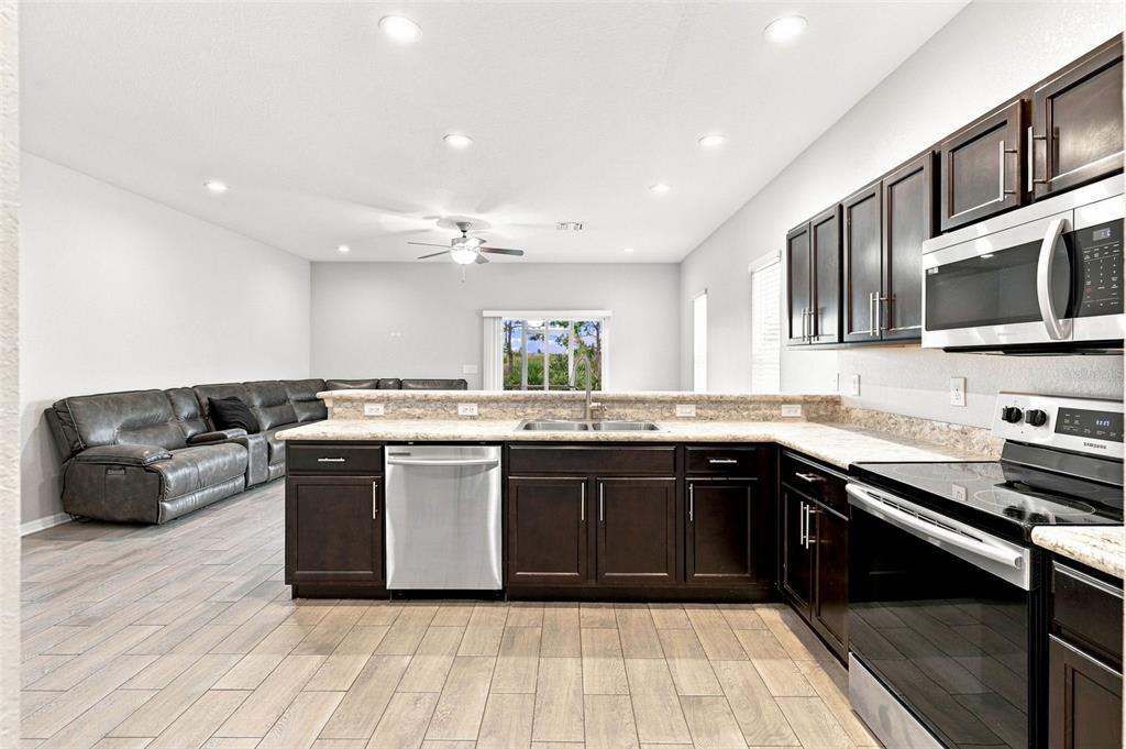 A kitchen with dark wood cabinets, stainless steel appliances, and an island facing a living area — 4641 VIGNETTE WAY, SARASOTA, FL