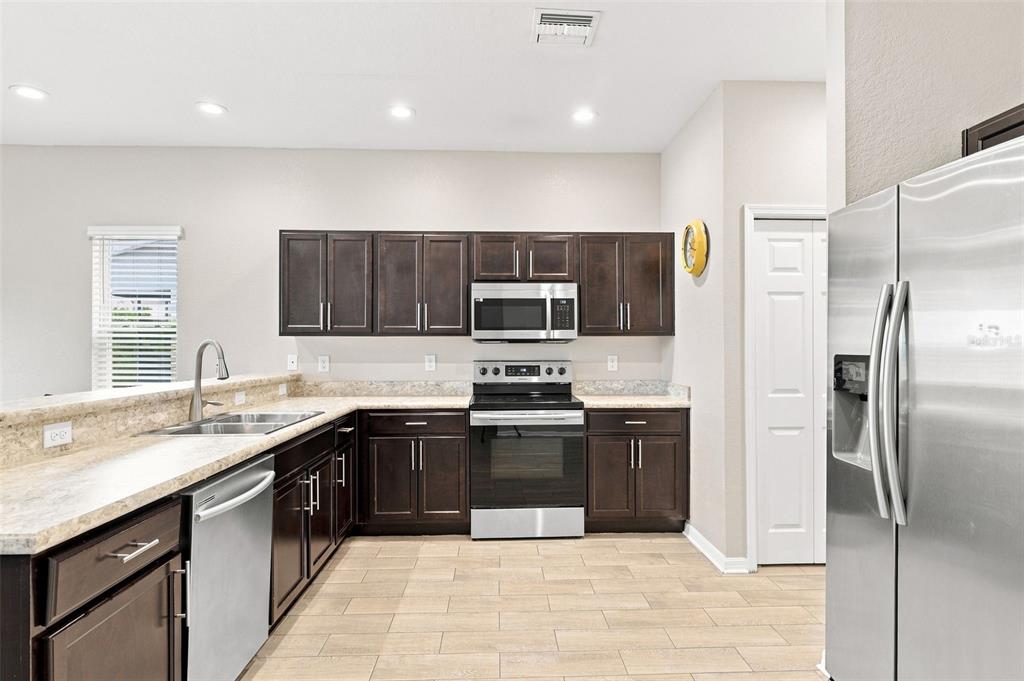 A kitchen with dark wood cabinets, stainless steel appliances, and light-colored countertops and flooring — 4641 VIGNETTE WAY, SARASOTA, FL