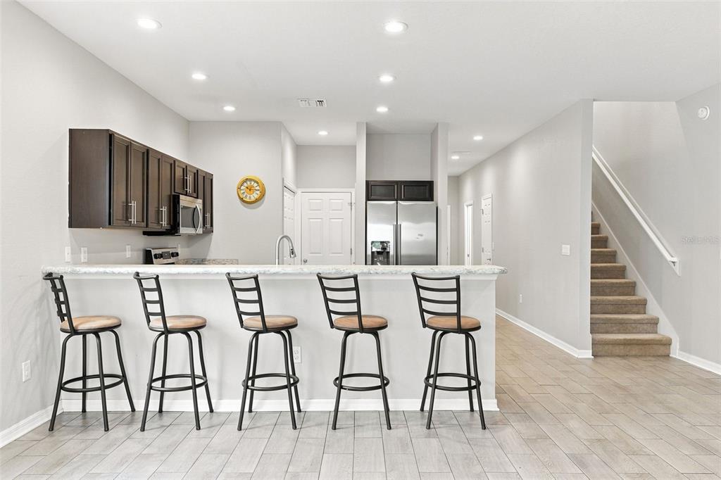 A kitchen with dark cabinets, stainless steel appliances, a breakfast bar, and an adjacent staircase — 4641 VIGNETTE WAY, SARASOTA, FL