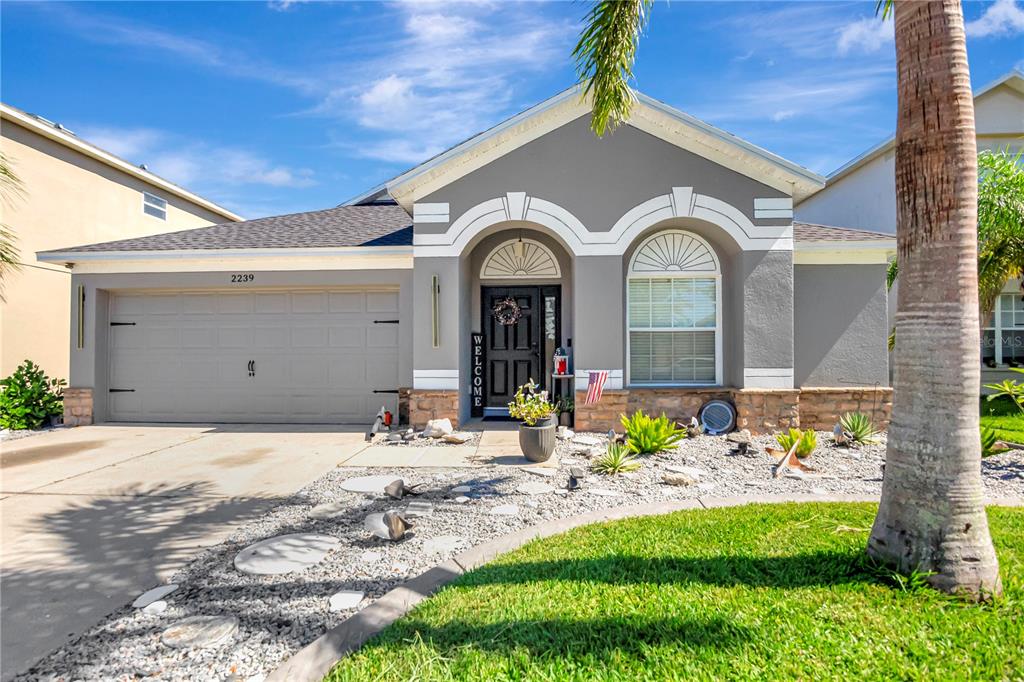 A gray single-story house with a two-car garage, stone accents, and a landscaped front yard — 2239 ROANOKE SPRINGS DRIVE, RUSKIN, FL