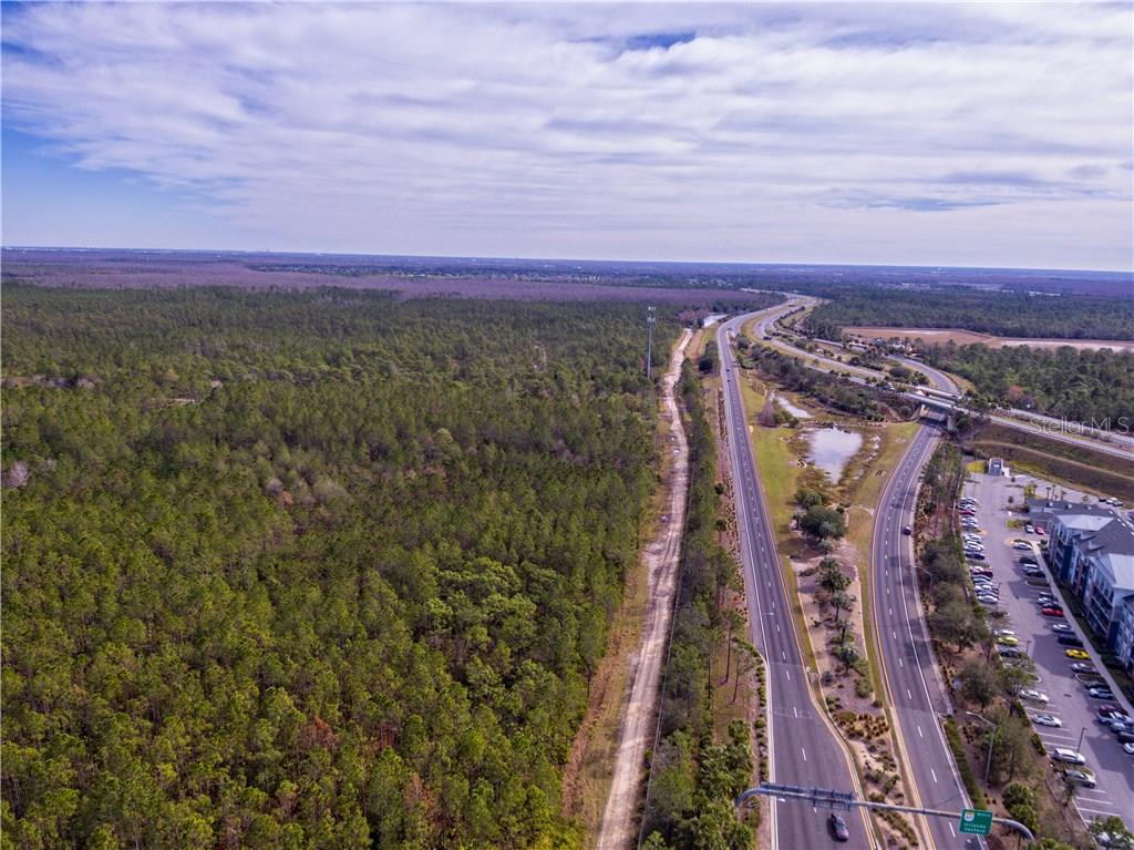 An aerial view shows a dense forest bordering a multi-lane highway and a modern apartment complex — INTERNATIONAL DRIVE, ORLANDO, FL