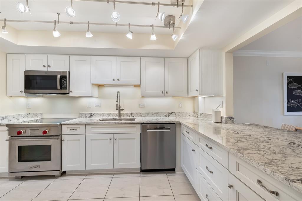 A kitchen features white cabinets, stainless steel appliances, and granite countertops under track lighting — 950 PALM AVENUE UNIT 304, BOCA GRANDE, FL