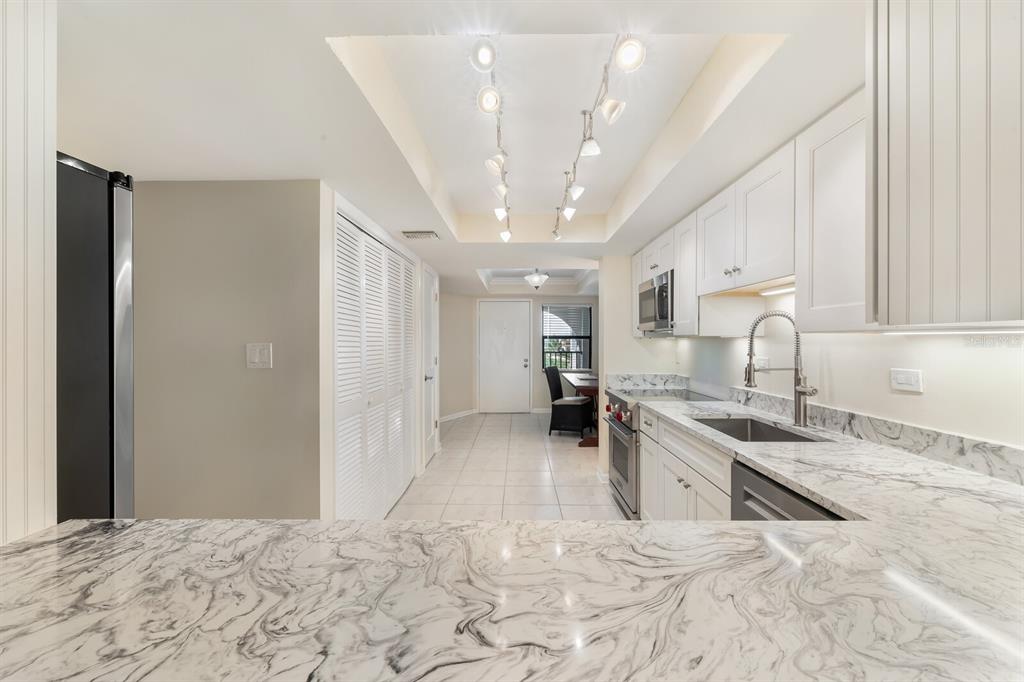 A kitchen with white cabinets, marble-patterned countertops, stainless steel appliances, and a track lighting fixture — 950 PALM AVENUE UNIT 304, BOCA GRANDE, FL