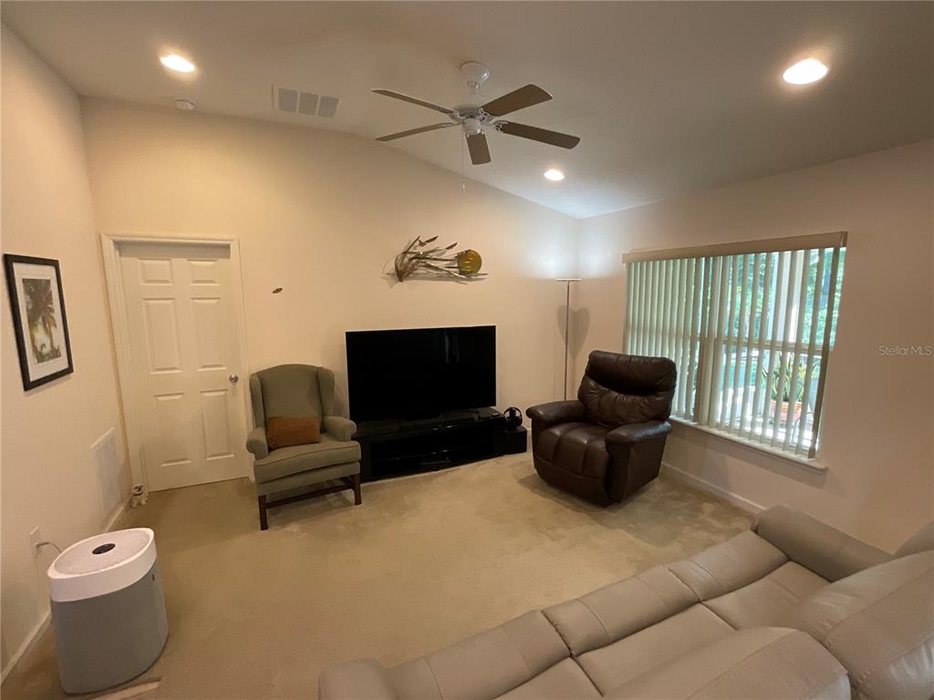 A living room features a vaulted ceiling, carpeted flooring, a television, and two armchairs — 151 PERGOLA PLACE, ORMOND BEACH, FL