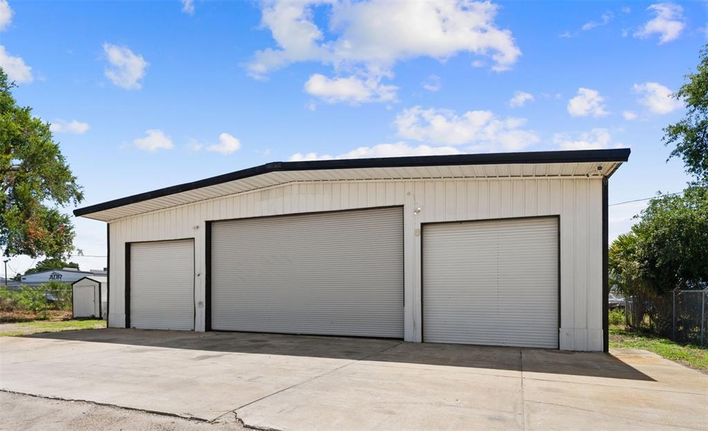 A white metal warehouse building features three roll-up garage doors and a concrete driveway — 12433 66TH STREET, LARGO, FL