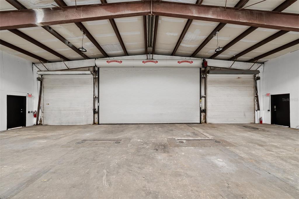 An industrial warehouse interior features three large roll-up doors and two black exit doors — 12433 66TH STREET, LARGO, FL