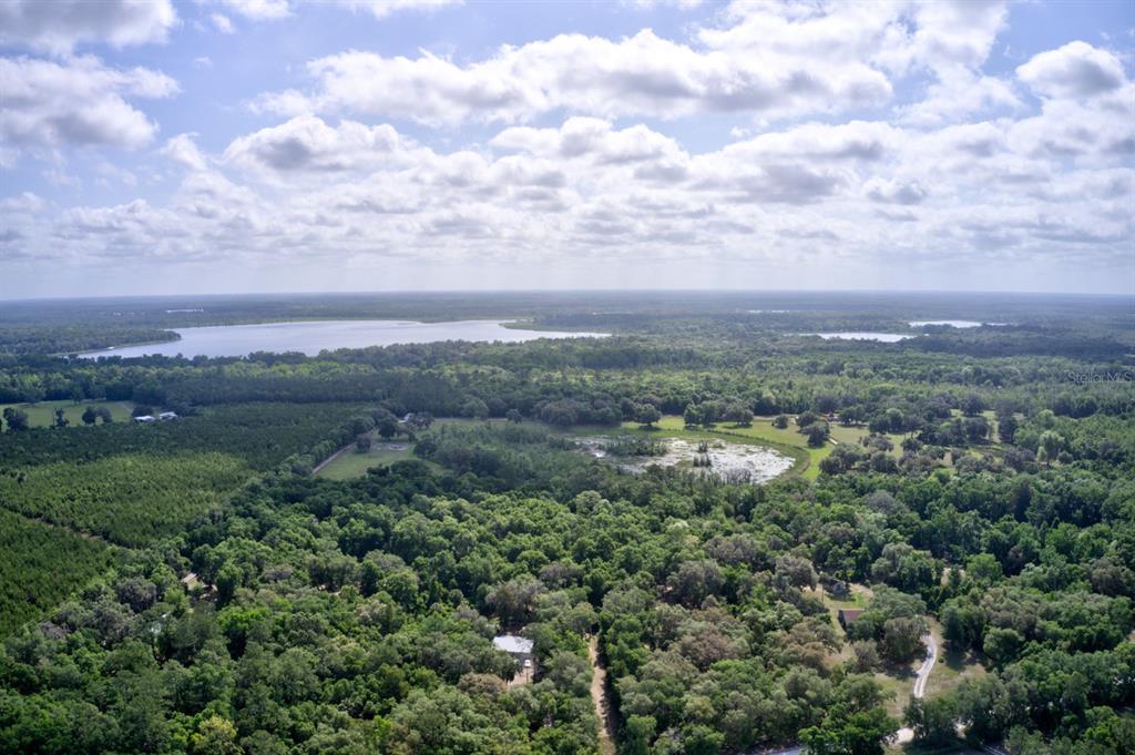 An aerial view shows a large forested property with a central pond and a distant lake — 8903 SE 225TH DRIVE, HAWTHORNE, FL
