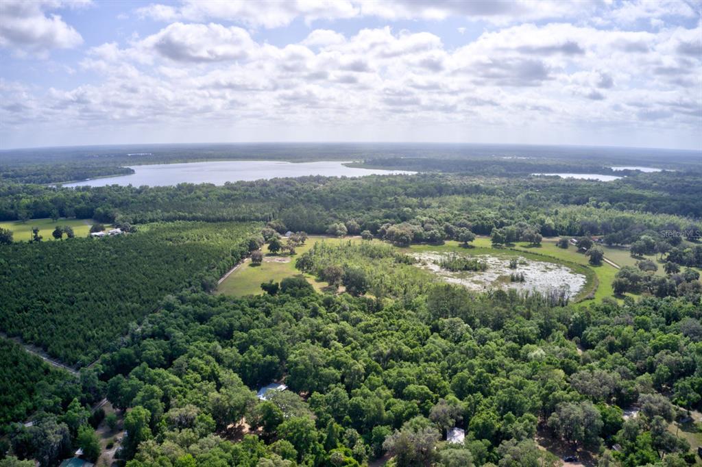 An aerial view shows a large, wooded property with a pond and a distant lake — 8903 SE 225TH DRIVE, HAWTHORNE, FL