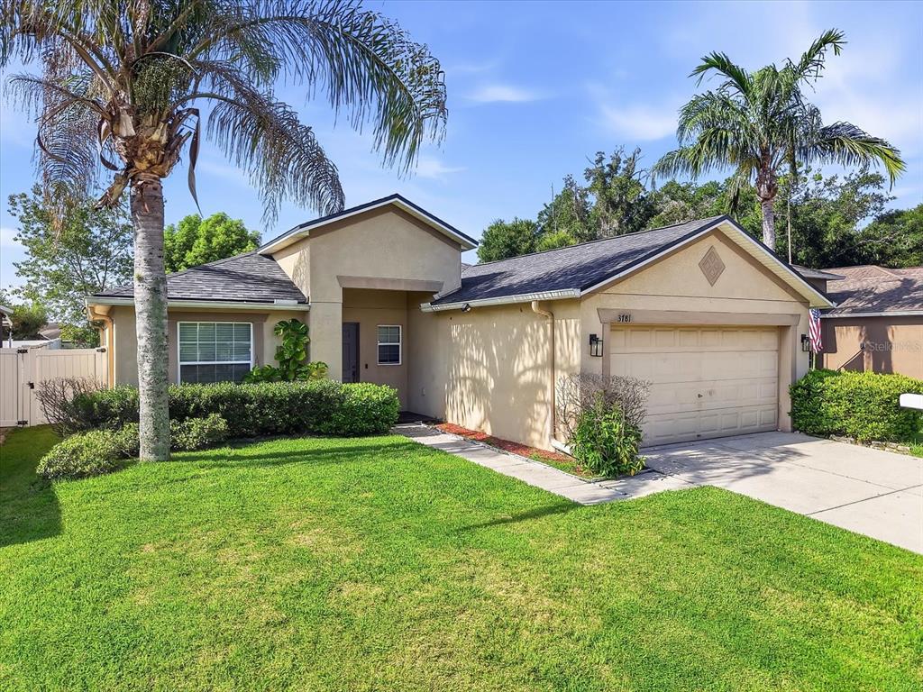 A single-story house with a tan stucco exterior, a two-car garage, and two palm trees — 3781 MADBURY CIRCLE, LAKELAND, FL