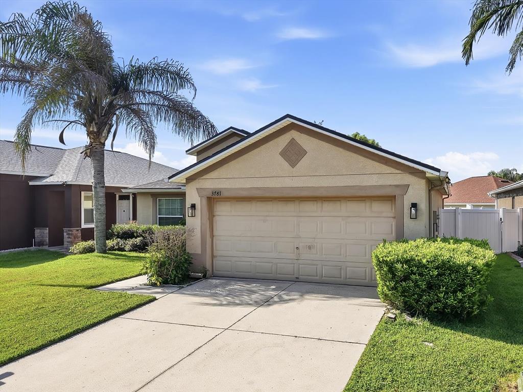 A single-story house with a beige stucco exterior, a two-car garage, and a palm tree — 3781 MADBURY CIRCLE, LAKELAND, FL
