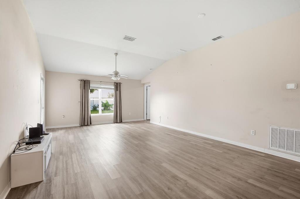 An empty living room features light-colored walls, wood-look flooring, a ceiling fan, and a window — 3781 MADBURY CIRCLE, LAKELAND, FL