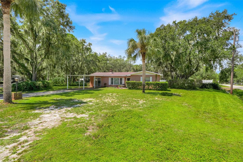 A single-story brick house with a carport sits on a grassy lot with trees — 11031 W BEACH PARKWAY, LAKE WALES, FL