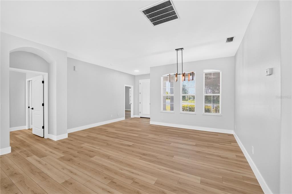 An empty room with light wood-look flooring, white walls, and a modern dining light fixture — 572 OCEANSIDE BOULEVARD, MELBOURNE, FL