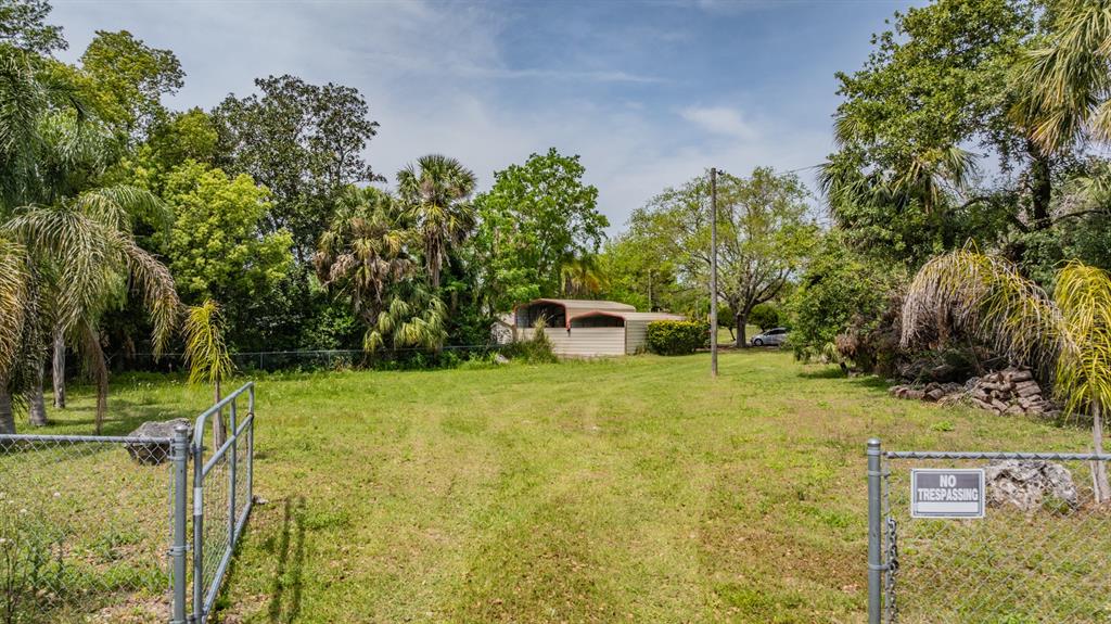 A grassy lot features a metal shed, mature trees, and a chain-link fence with a gate — 0 VILLA DRIVE, HUDSON, FL