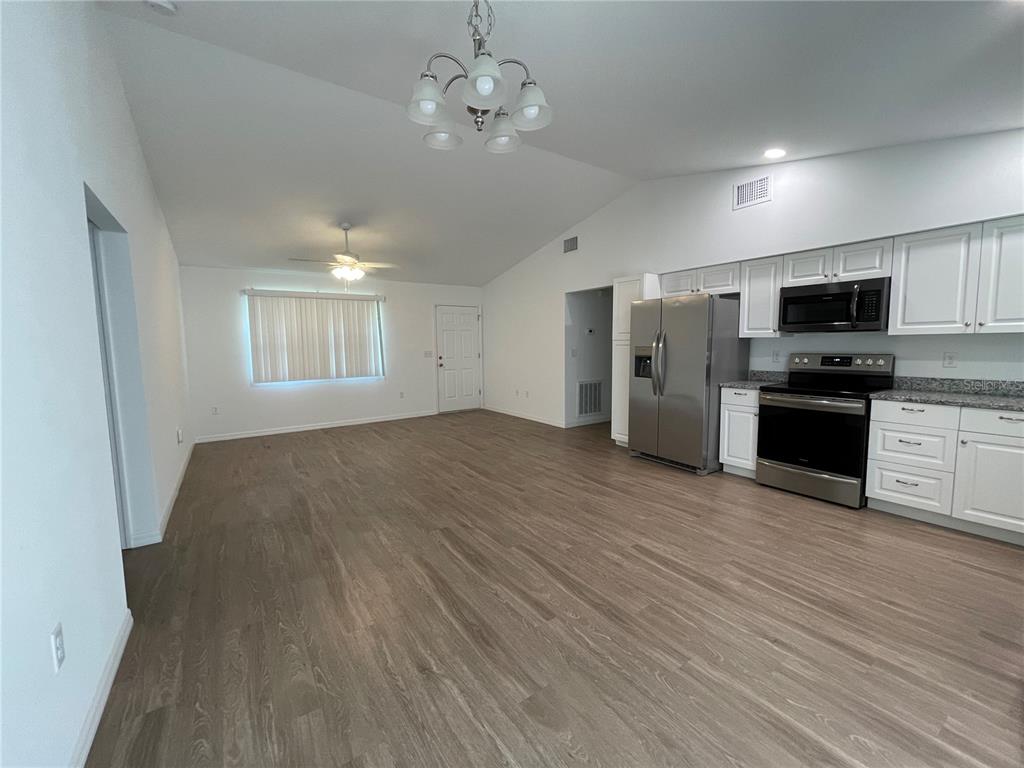 An open-concept kitchen and living area features white cabinetry, stainless steel appliances, and wood-look flooring — 2811 GARFIELD STREET W, INVERNESS, FL