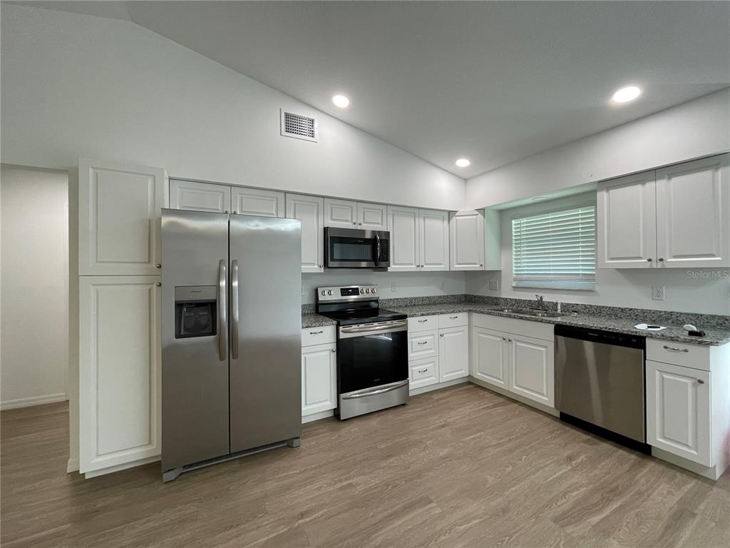 A kitchen features white cabinets, stainless steel appliances, and granite countertops over wood-look flooring — 2811 GARFIELD STREET W, INVERNESS, FL