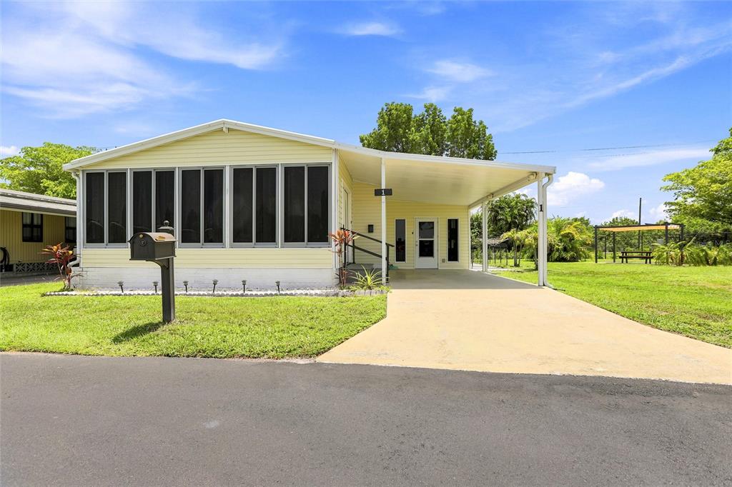 A light yellow manufactured home features a screened-in porch and a covered carport — 1 POINSETTIA DRIVE, FORT MYERS, FL