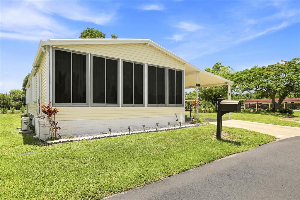 A light yellow mobile home with a screened-in porch and a carport sits on grass — 1 POINSETTIA DRIVE, FORT MYERS, FL