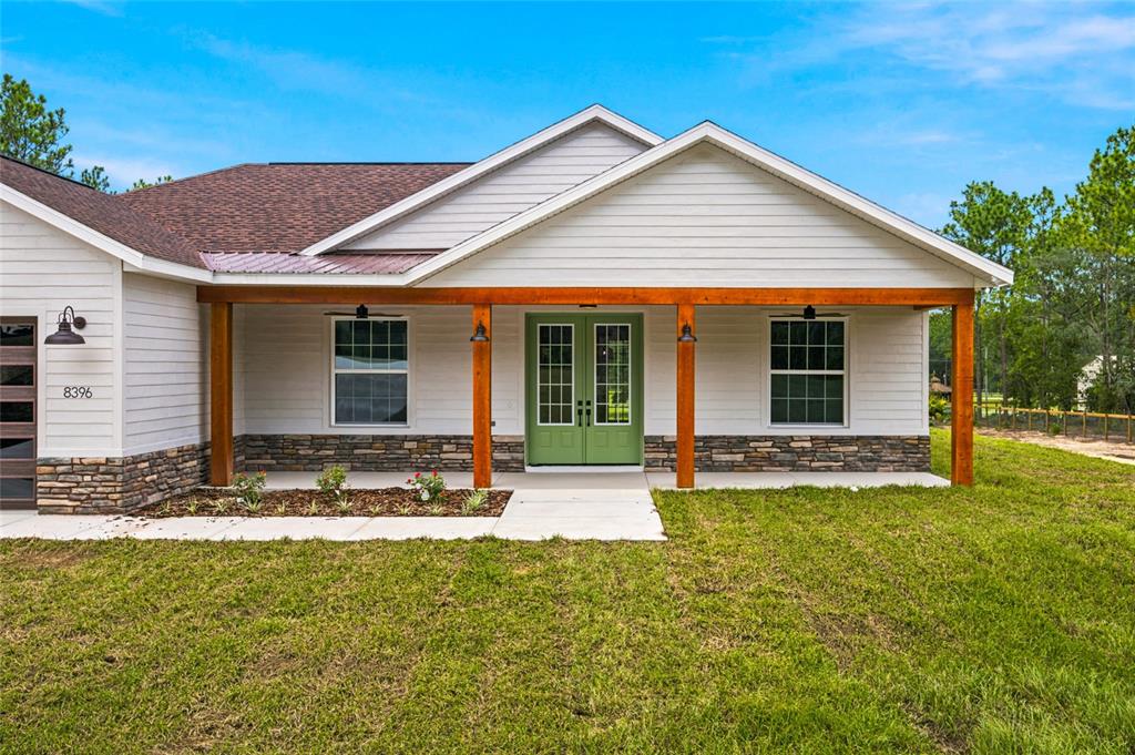 A single-story house features a covered porch with wooden posts and a green double door — 8396 SW 125TH CT ROAD, DUNNELLON, FL