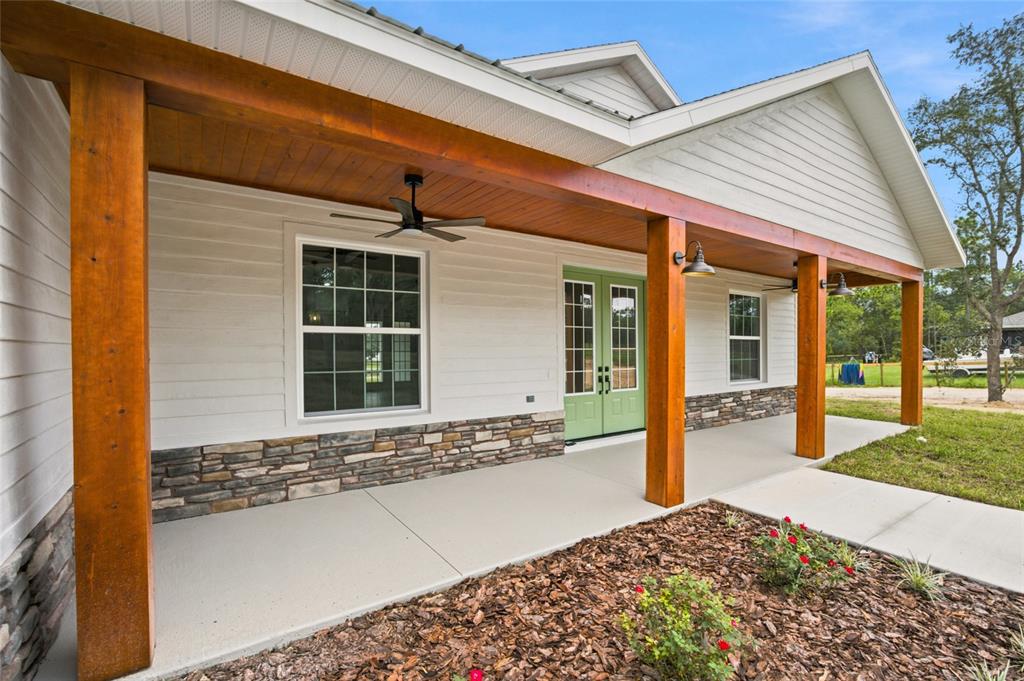 A white farmhouse exterior features a covered porch with wood posts, stone accents, and green doors — 8396 SW 125TH CT ROAD, DUNNELLON, FL