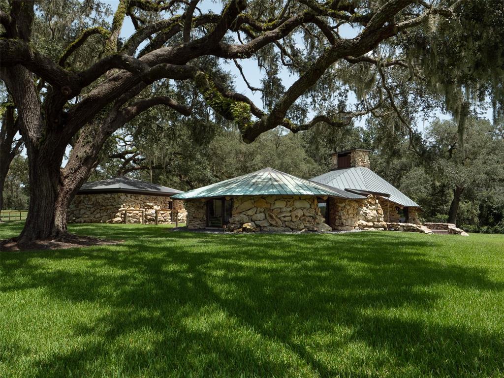 A stone house with a metal roof sits on a grassy lawn under large trees — 8351 NW 110TH STREET, REDDICK, FL