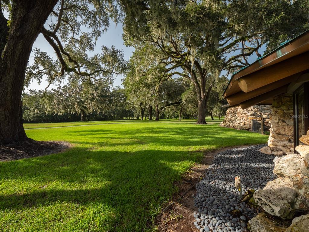 A grassy yard with large oak trees sits beside a stone-walled building with an overhang — 8351 NW 110TH STREET, REDDICK, FL