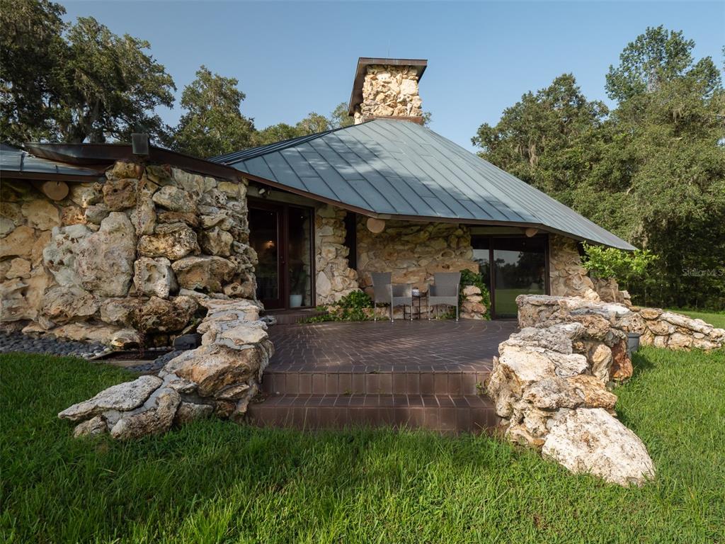 A stone-walled house with a metal roof features a brick patio and outdoor seating area — 8351 NW 110TH STREET, REDDICK, FL
