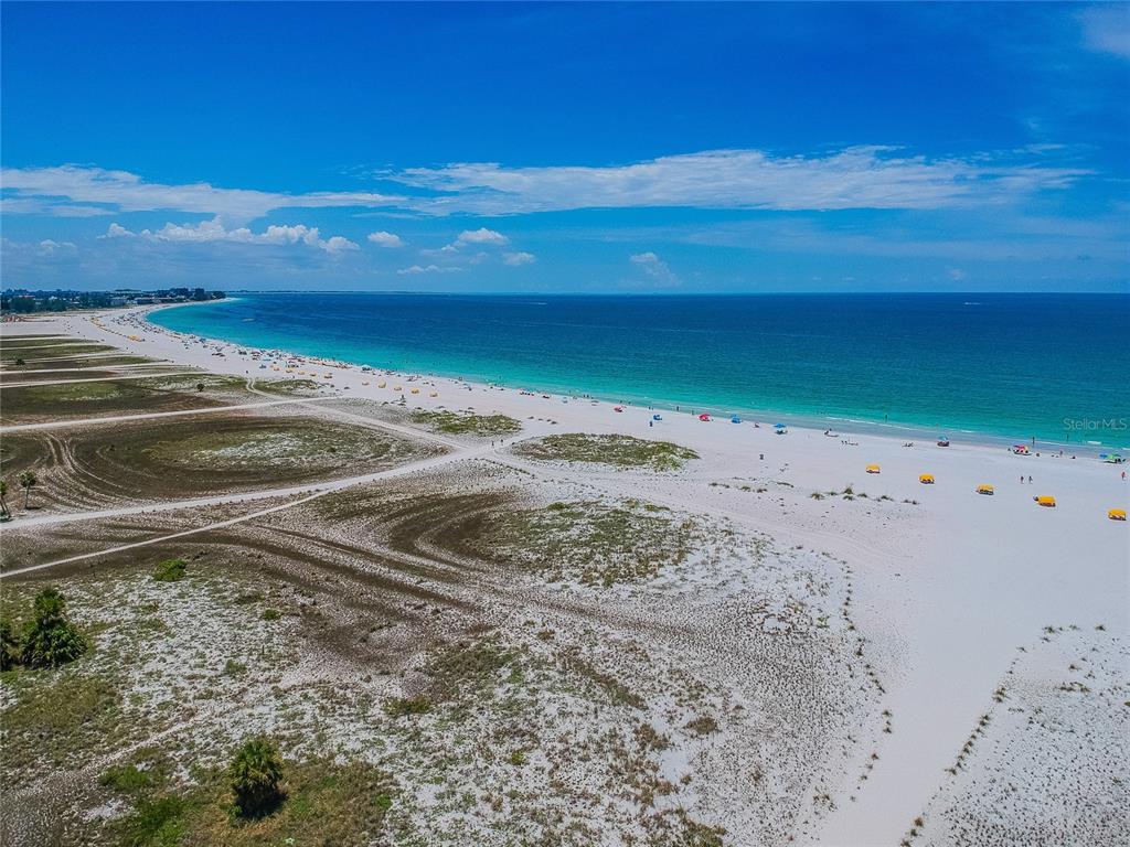 A balcony with two chairs and a small table overlooks a street and the ocean — 11605 GULF BOULEVARD UNIT 502, TREASURE ISLAND, FL