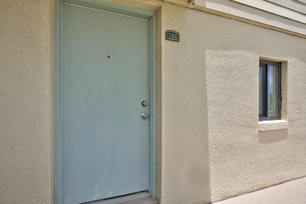 A light green door with a number 150 sign and a window on a stucco wall — 8550 A1A S UNIT 14250, ST AUGUSTINE, FL