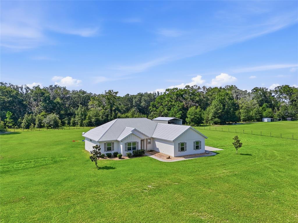 A white single-story house with a metal roof sits in a large, open grassy field — 5600 SW COUNTY ROAD 240, LAKE CITY, FL