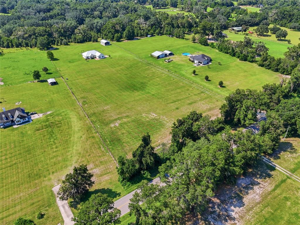 An aerial view shows several houses and outbuildings situated on large, grassy rural lots — 5600 SW COUNTY ROAD 240, LAKE CITY, FL