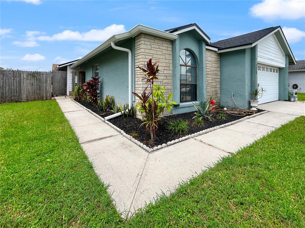 A teal house with stone veneer accents, a concrete walkway, and a landscaped front garden — 3228 RUNNING BEAR WAY, KISSIMMEE, FL