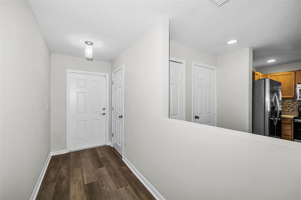 An entryway with wood-look flooring leads to a white front door and a kitchen pass-through — 8013 SUTTON TERRACE LANE, TAMPA, FL