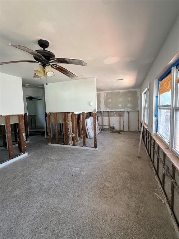 An interior room under renovation with exposed wall studs, concrete flooring, and a ceiling fan — 13434 1ST ST E, MADEIRA BEACH, FL
