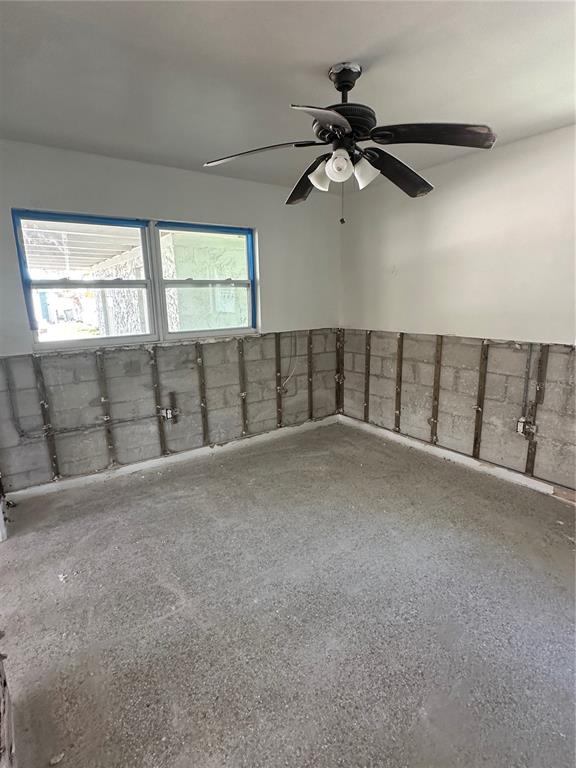 An unfinished room features exposed concrete block walls, metal furring strips, and a ceiling fan — 13434 1ST ST E, MADEIRA BEACH, FL