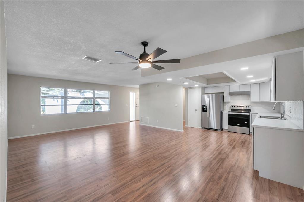 An open-concept living area features wood-look flooring, a ceiling fan, and a white kitchen — 1995 MEADOW DRIVE, CLEARWATER, FL