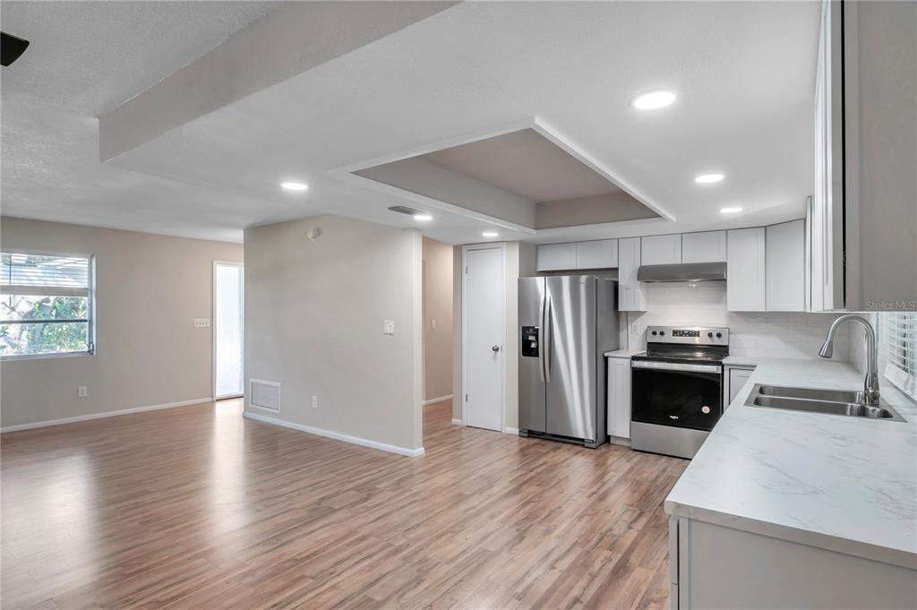 A kitchen with stainless steel appliances and white cabinets opens into a living area — 1995 MEADOW DRIVE, CLEARWATER, FL