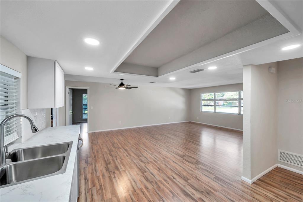 A kitchen sink overlooks an open-concept living area with wood-look flooring and a tray ceiling — 1995 MEADOW DRIVE, CLEARWATER, FL