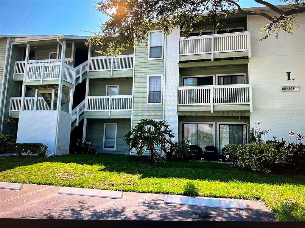 A three-story apartment building with light green siding, white railings, and a parking lot foreground — 455 ALT 19 S UNIT 202, PALM HARBOR, FL