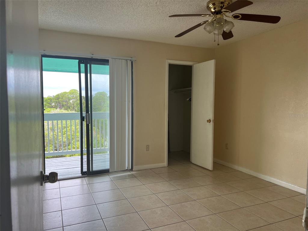 A bedroom with tile flooring, a ceiling fan, a walk-in closet, and a sliding glass door — 455 ALT 19 S UNIT 202, PALM HARBOR, FL