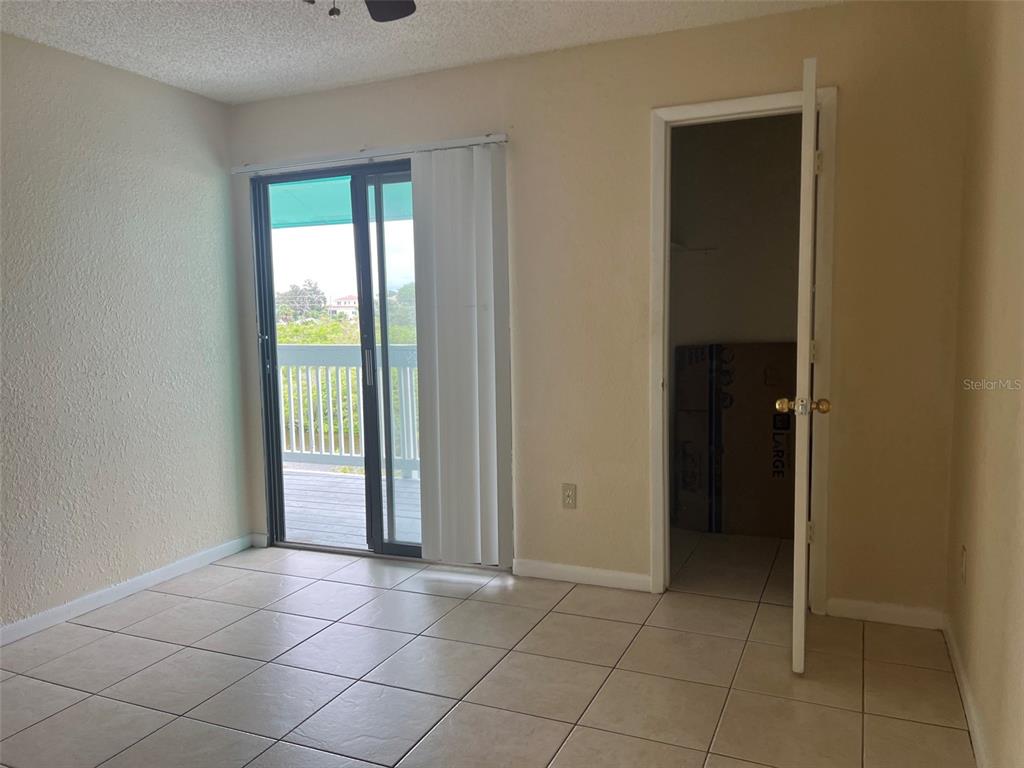 A room with beige walls, tile flooring, a sliding glass door, and an open closet — 455 ALT 19 S UNIT 202, PALM HARBOR, FL