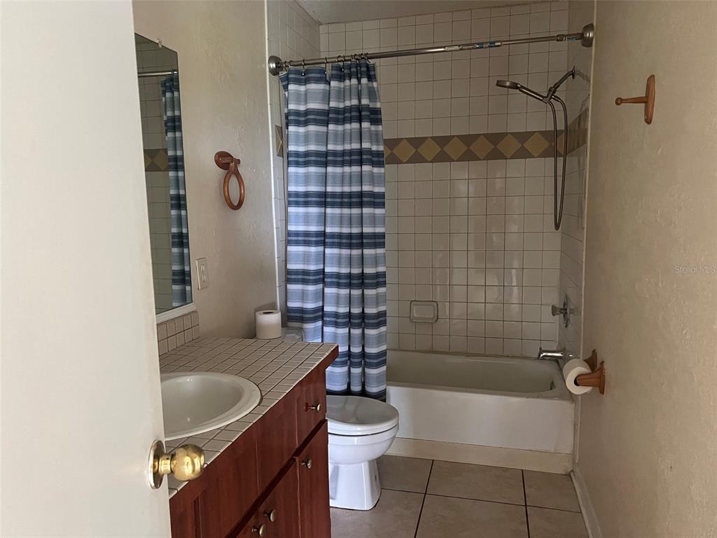 A bathroom features a tiled vanity, a toilet, and a shower-tub combination with a curtain — 455 ALT 19 S UNIT 202, PALM HARBOR, FL
