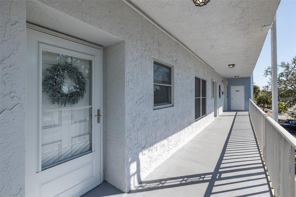 An exterior walkway of a multi-story building features white stucco walls and a white door — 4939 FLORAMAR TERRACE UNIT 312, NEW PORT RICHEY, FL